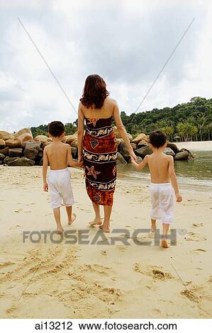 Stock Image - Mother with two boys, walking on beach, rear view. Fotosearch