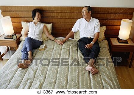 Stock Photo - Older couple lying on bed, holding hands. Fotosearch