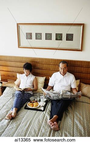 Older couple lying on bed, reading newspaper, tray of food between them View Large Photo Image Stock Photography - Older couple lying on bed, reading newspaper, tray of food between them. Fotosearch