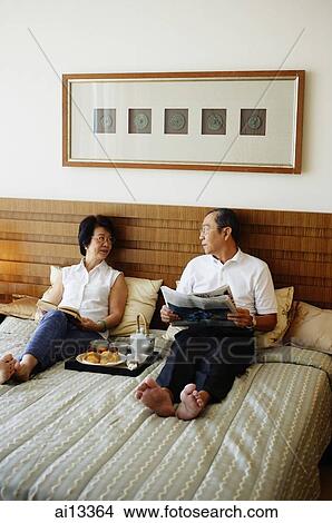 Older couple lying on bed, tray of food between them View Large Photo Image Picture - Older couple lying on bed, tray of food between them. Fotosearch