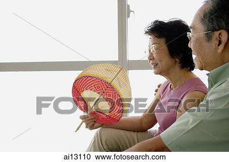 Senior couple sitting down, woman holding fan View Large Photo Image Stock Image - Senior couple sitting down, woman holding fan. Fotosearch