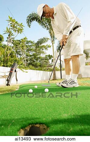 Stock Image - Senior man playing golf on putting green. Fotosearch