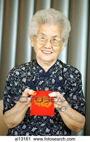 Senior woman holding red envelope with "wealth" script, looking at camera View Large Photo Image Stock Image - Senior woman holding red envelope with "wealth" script, looking at camera. Fotosearch
