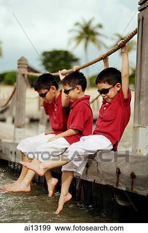 Stock Photo - Three boys sitting on jetty. Fotosearch