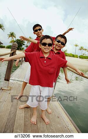Three boys standing in a row, arms outstretched View Large Photo Image Stock Photograph - Three boys standing in a row, arms outstretched. Fotosearch