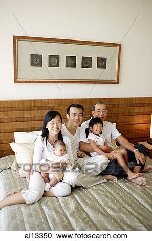 Stock Image - Three generation family on bed, looking at camera. Fotosearch