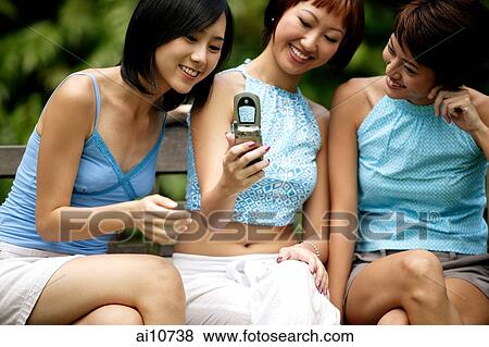 Three young women sitting side by side, using camera phone, posing View Large Photo Image Stock Photo - Three young women sitting side by side, using camera phone, posing. Fotosearch