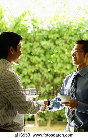 Two businessmen shaking hands, holding cups and saucers View Large Photo Image Stock Photo - Two businessmen shaking hands, holding cups and saucers. Fotosearch