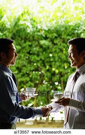 Two businessmen with cups and saucers, shaking hands View Large Photo Image Stock Photo - Two businessmen with cups and saucers, shaking hands. Fotosearch
