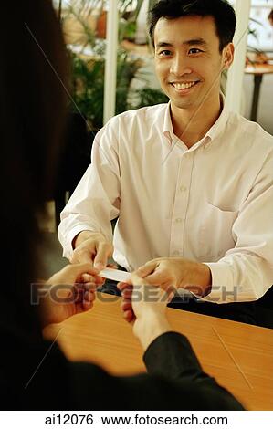 Two executives sitting across desk, exchanging business card View Large Photo Image Stock Photograph - Two executives sitting across desk, exchanging business card. Fotosearch