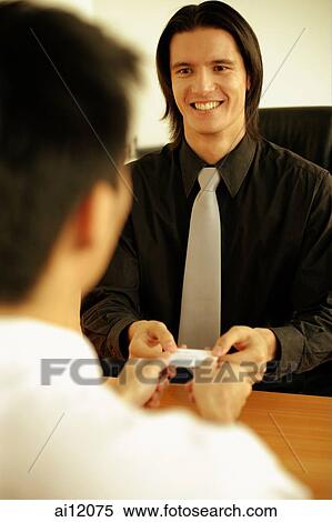 Two executives sitting across desk, exchanging business card View Large Photo Image Stock Photography - Two executives sitting across desk, exchanging business card. Fotosearch