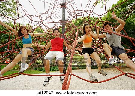 Stock Image - Two women and two men, holding on to rope on jungle gym, looking at camera. Fotosearch