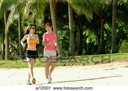 Stock Photo - Two women jogging along beach, side by side. Fotosearch