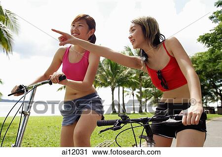 Stock Image - Two women on bicycles, one woman pointing. Fotosearch