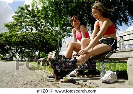 Two women sitting side by side on park bench wearing roller blades View Large Photo Image Stock Photo - Two women sitting side by side on park bench wearing roller blades. Fotosearch