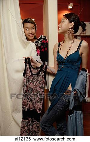 Stock Photography - Two women trying on clothes at shop, one behind curtain. Fotosearch