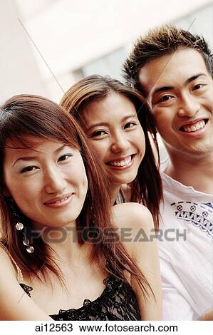 Two young women and one young man, looking at camera, smiling View Large Photo Image Stock Image - Two young women and one young man, looking at camera, smiling. Fotosearch