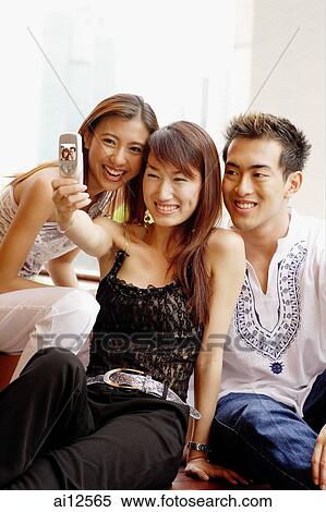 Two young women and one young man looking at camera phone View Large Photo Image Stock Photography - Two young women and one young man looking at camera phone. Fotosearch