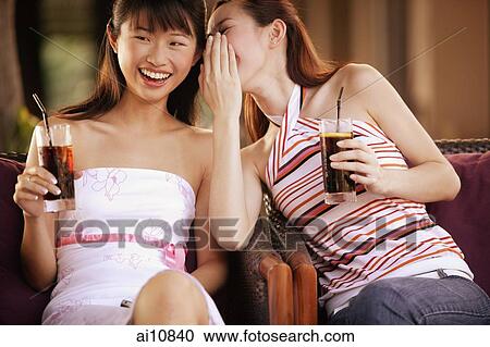 Two young women holding drinks, sitting side by side, whispering View Large Photo Image Stock Image - Two young women holding drinks, sitting side by side, whispering. Fotosearch