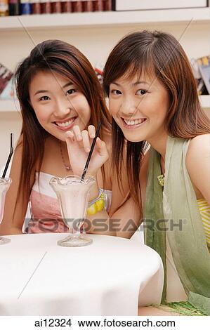 Picture -  Two young women, looking at camera, drinking milkshakes. Fotosearch