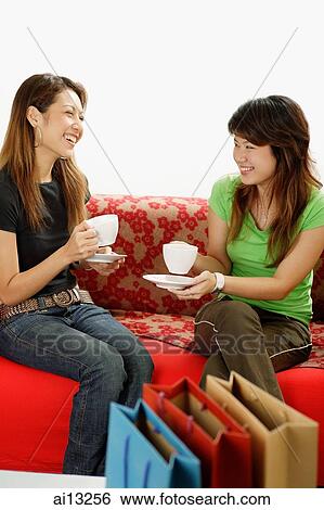 Two young women, sitting on sofa, drinking tea View Large Photo Image Stock Photograph - Two young women, sitting on sofa, drinking tea. Fotosearch