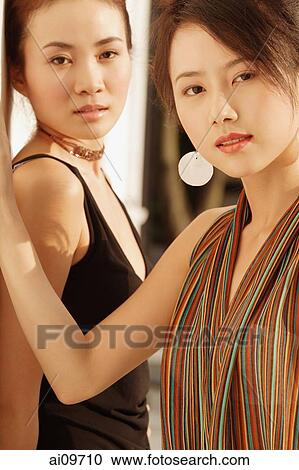 Two young women standing looking at camera View Large Photo Image Stock Image - Two young women standing looking at camera. Fotosearch
