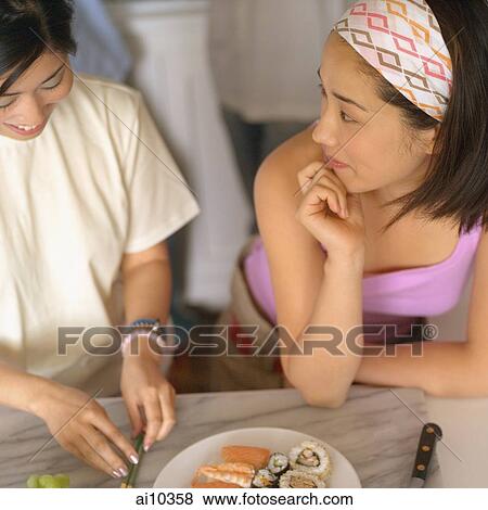 Two young women talking, one slicing fruit View Large Photo Image Stock Photo - Two young women talking, one slicing fruit. Fotosearch