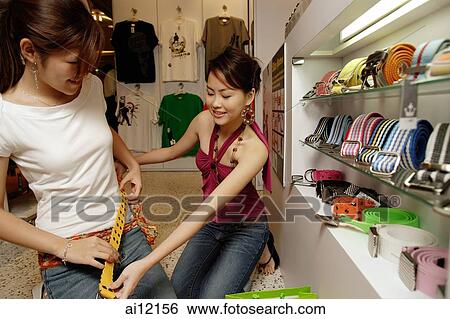 Two young women trying on belts in shop View Large Photo Image Stock Photograph - Two young women trying on belts in shop. Fotosearch