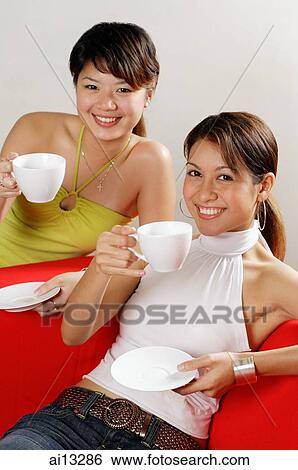 Two young women with cups and saucers, looking at camera View Large Photo Image Stock Photograph - Two young women with cups and saucers, looking at camera. Fotosearch