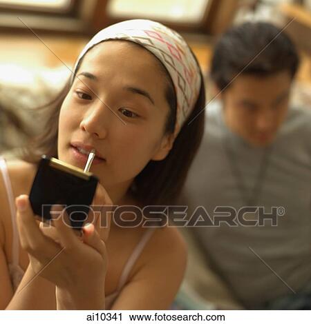 Woman applying lipstick, man in the background View Large Photo Image Stock Image - Woman applying lipstick, man in the background. Fotosearch