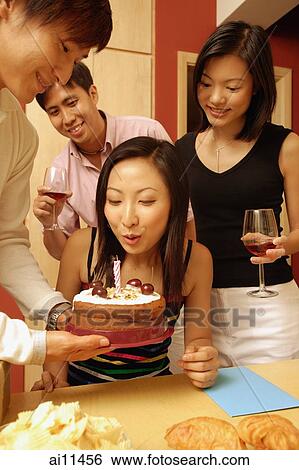 Woman blowing out candle on cake, surrounded by friends View Large Photo Image Stock Photograph - Woman blowing out candle on cake, surrounded by friends. Fotosearch