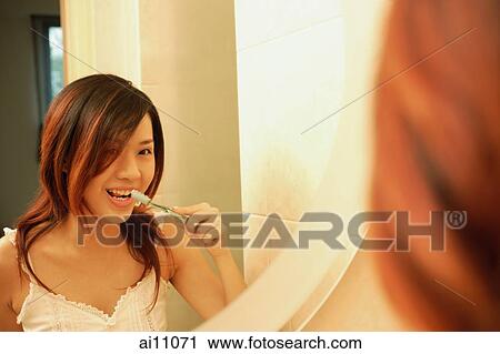 Woman brushing her teeth, looking at mirror View Large Photo Image Stock Image - Woman brushing her teeth, looking at mirror. Fotosearch
