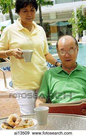 Stock Photo - Woman holding coffee mug, man sitting down looking at newspaper. Fotosearch