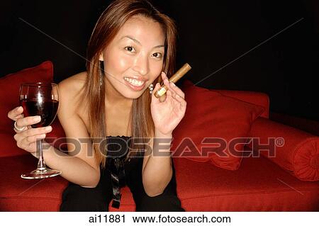 Stock Image - Woman holding wine glass and cigar, looking at camera. Fotosearch
