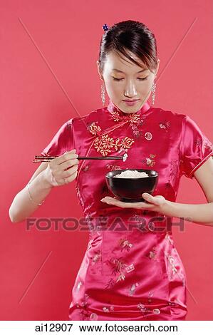 Woman in Cheongsam, holding bowl of rice and chopsticks, looking down View Large Photo Image Stock Photo - Woman in Cheongsam, holding bowl of rice and chopsticks, looking down. Fotosearch