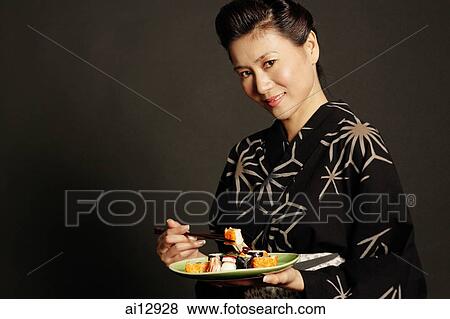 Woman in Japanese costume, holding chopsticks and a plate of Japanese food View Large Photo Image Stock Photo - Woman in Japanese costume, holding chopsticks and a plate of Japanese food. Fotosearch