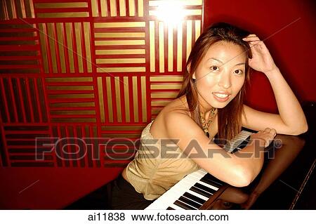 Stock Photo - Woman leaning on piano, looking at camera. Fotosearch