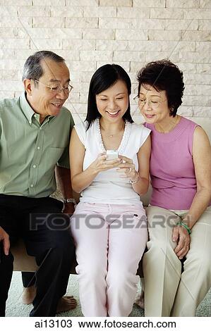 Woman looking at mobile phone, sitting between older couple View Large Photo Image Stock Image - Woman looking at mobile phone, sitting between older couple. Fotosearch