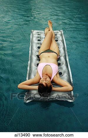 Stock Image - Woman lying on inflatable bed in swimming pool. Fotosearch