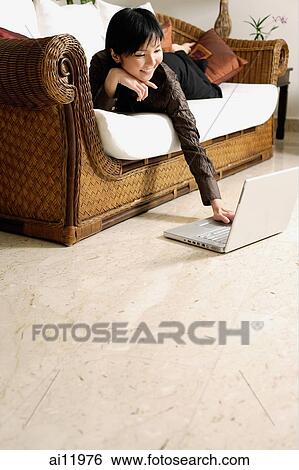 Woman lying on sofa, using laptop View Large Photo Image Stock Photograph - Woman lying on sofa, using laptop. Fotosearch