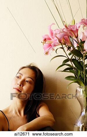 Stock Image - Woman next to vase with flowers, looking away. Fotosearch