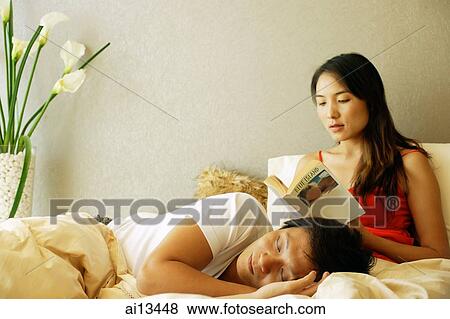 Stock Photo - Woman on bed, reading a book, man lying on her lap. Fotosearch