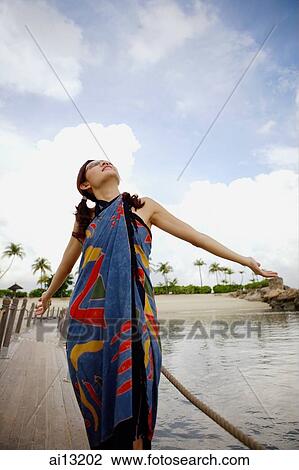 Stock Image - Woman on jetty, looking up, hands outstretched. Fotosearch