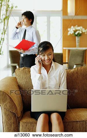 Woman on sofa, using laptop and mobile phone, man in the background View Large Photo Image Stock Image - Woman on sofa, using laptop and mobile phone, man in the background. Fotosearch