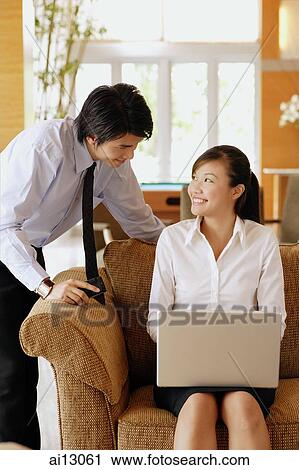 Woman on sofa, using laptop, man leaning over View Large Photo Image Stock Image - Woman on sofa, using laptop, man leaning over. Fotosearch