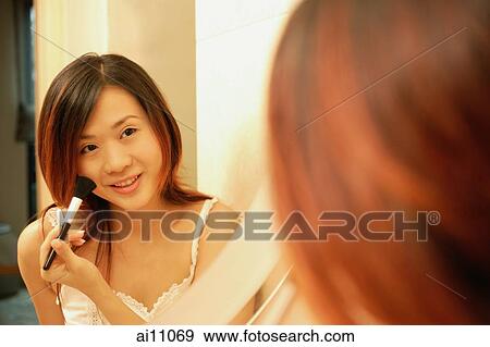 Stock Photo - Woman putting on mascara, looking at mirror. Fotosearch