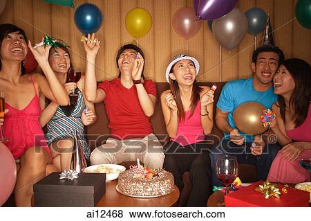 Stock Photo - Young adults celebrating, looking up at balloons. Fotosearch