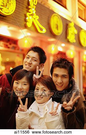 Stock Photograph - Young adults smiling at camera making peace signs. Fotosearch