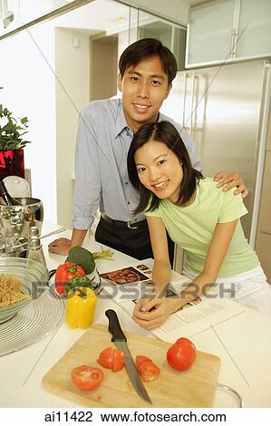 Stock Image - Young adults standing in kitchen, side by side, looking at camera. Fotosearch