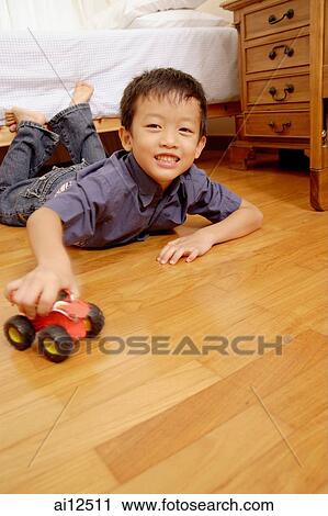 Stock Image - Young boy lying on floor with toy, looking at camera. Fotosearch